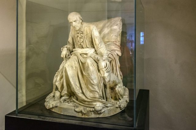 “The philosopher on the throne”, a sculpture showing the aged Prussian King Frederick II (called “The Old Fritz”) with his favourite dogs. Displayed in the vaults of Hohenzollern castle, Bisinge. Photo by Dr. Zeltsam CC BY SA 4.0