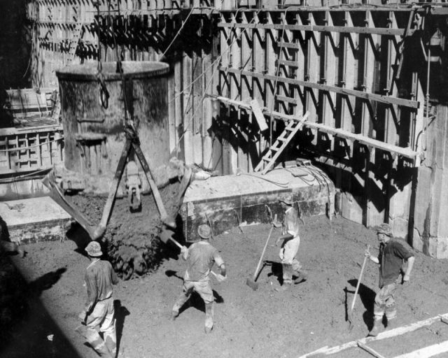 Concrete sluices from a bucket to a form at Hoover Dam, workers prepare to flatten out the pour.