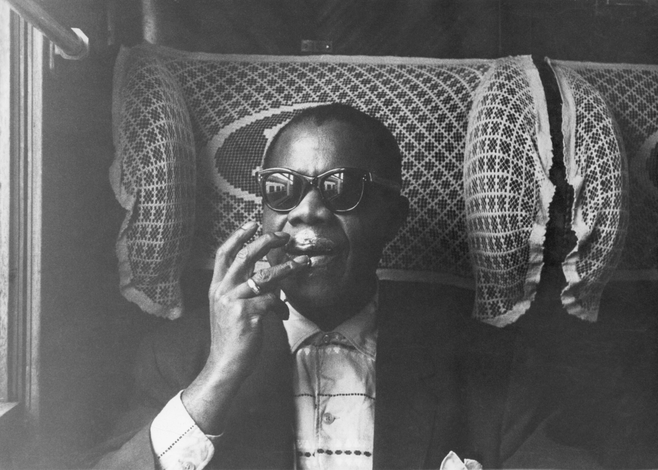 Louis Armstrong wearing sunglasses on train, moisturizing his lips