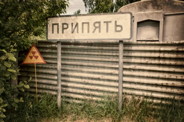 The Pripyat City sign in Chernobyl restricted zone with radioactivity warning sign.