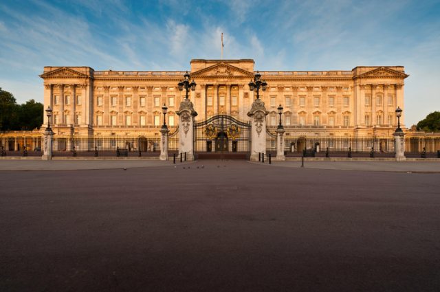 London, UK – May 3, 2011: Warm dawn sunlight illuminates the Portland stone facade, windows, balcony and ornate entrance gates of Buckingham Palace, London residence of the British Monarch, from the Victoria Memorial on The Mall.