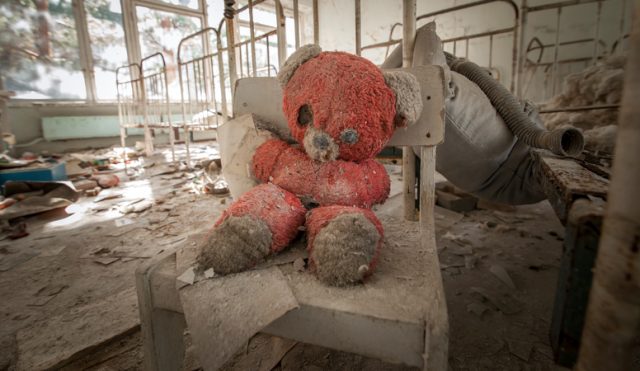 Old red teddy bear sitting on a chair in an abandoned kindergarten in Pripyat – Chernobyl Nuclear Power Plant Zone of Alienation.