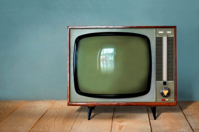 Vintage TV set on wooden table against old blue wall background.