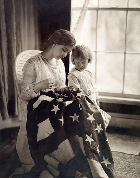 A child watches as a woman sews a star on a United States flag.