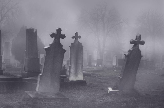 Old creepy haunted cemetery on misty night.