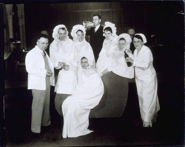Jessie Tarbox Beals (dressed as a nurse) and seven unidentified men dressed up as babies and doctors.