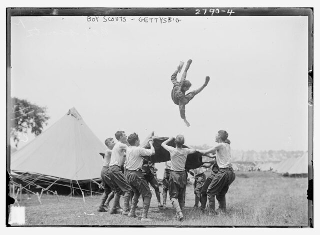 Group of boy scouts flinging a fellow scout into the air