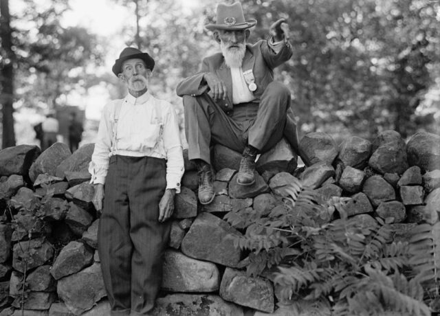 One man leaning against a stone fence while another sits atop it