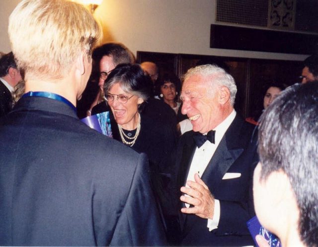 Anne Bancroft and Mel Brooks talking to Bette Midler who is obscured by the man on the left. The photo has been taken at the 49th Emmy Awards in 1997. Photo by Alan Light CC BY 2.0