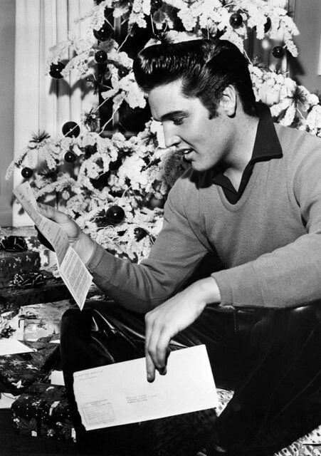 Elvis Presley reading a letter in front of a Christmas tree