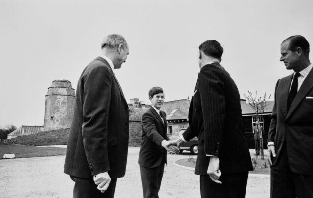 Then-Prince Charles shaking hands with a Gordonstoun school official while another man and Prince Philip stand nearby