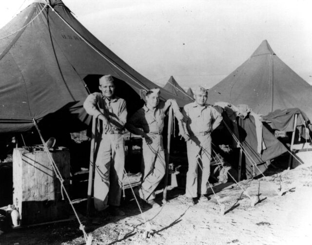 Edmond John, Wilsie Bitsei and Eugene Crawford standing outside of a tent