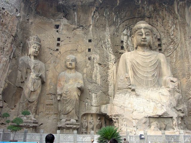 The Fengxian cave (c. 675 AD) of the Longmen Grottoes, commissioned by Wu Zetian; the large, central Buddha is representative of the Vairocana. Photo by G41rn8 CC BY-SA 4.0