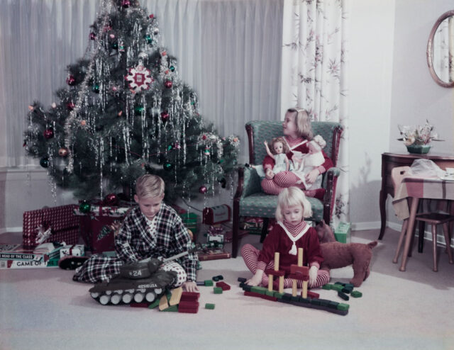 Children playing with their presents by the Christmas tree