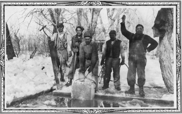 Five men cut large blocks of ice from a frozen lake.