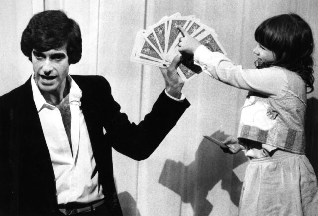 David Copperfield holding cards, and young girl  pointing at one.