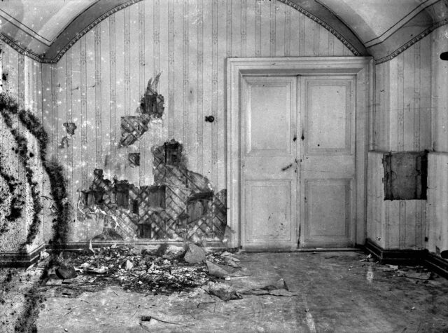 A wall with a door, damaged by gunfire.