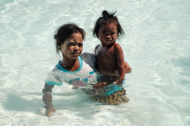 Semporna, Sabah / Malaysia – June 5, 2017: local bajau tribal member mother with her daughter swimming in the crystal clear sea around a white sandy beach.