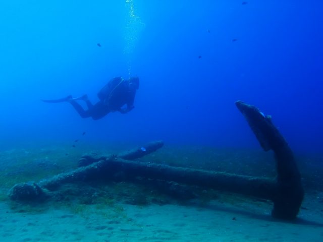 A scuba diver looks at a huge anchor.