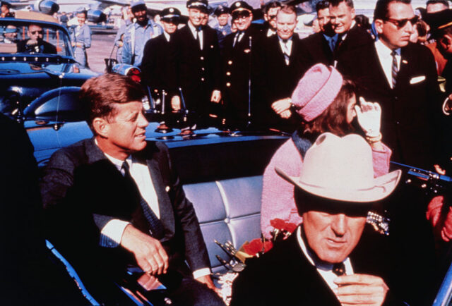 Jackie and John F. Kennedy sitting in the back of a vehicle, while John Connally sits in the front passenger seat