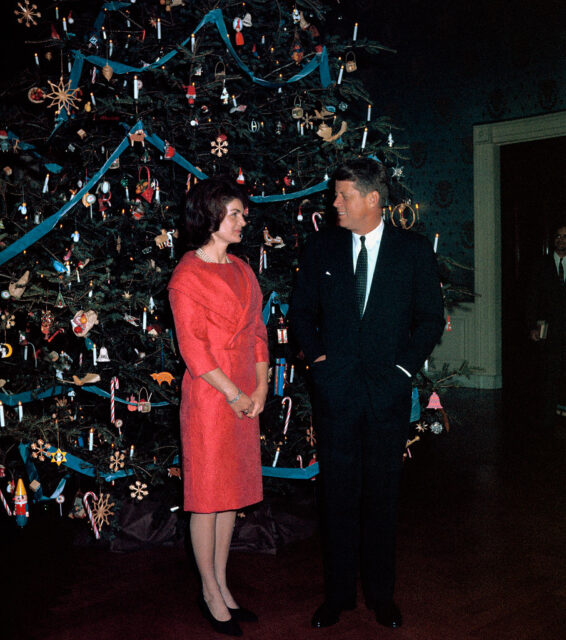John F. and Jacqueline Kennedy staring at each other while standing in front of a Christmas tree