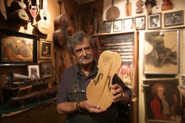 76-year-old Israeli violin maker Amnon Weinstein holds a violin that survived the Second World War bearing German writing and a Nazi Swastika sign at his workshop in Tel Aviv on July 15, 2016. Photo by MENAHEM KAHANA/AFP/Getty Images