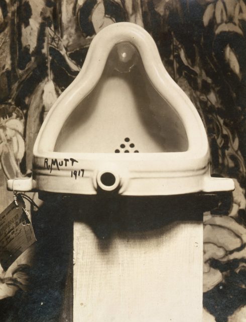 Marcel Duchamp Fountain, 1917, photograph by Alfred Stieglitz at 291 (art gallery) following the 1917 Society of Independent Artists exhibit, with entry tag visible. The backdrop is The Warriors by Marsden Hartley.