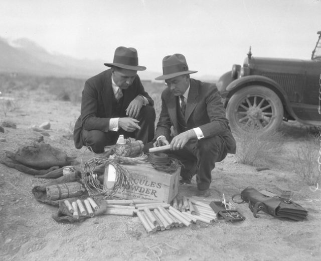 Two men examining a kit of dynamite and wire found during sabotage incidents of Owens Valley Aqueduct, Southern California, c. 1924.