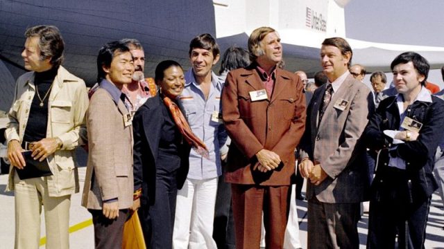 The Space Shuttle Enterprise rolls out of the Palmdale manufacturing facilities with Star Trek television cast and crew members. From left to right, the following are pictured: DeForest Kelley, who portrayed Dr. “Bones” McCoy on the series; George Takei (Mr. Sulu); James Doohan (Chief Engineer Montgomery “Scotty” Scott); Nichelle Nichols (Lt. Uhura); Leonard Nimoy (Mr. Spock); series creator Gene Roddenberry; NASA Deputy Administrator George Low; and, Walter Koenig (Ensign Pavel Chekov).