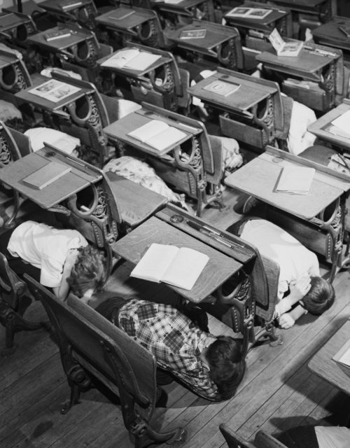 School children learn to protect themselves in case of nuclear attack by practicing a duck and cover drill in the classroom of their school.