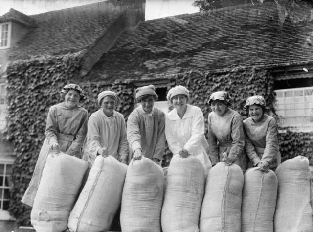 A group of smiling female workers pose with sacks of flour in the grounds of a British mill during the First World War