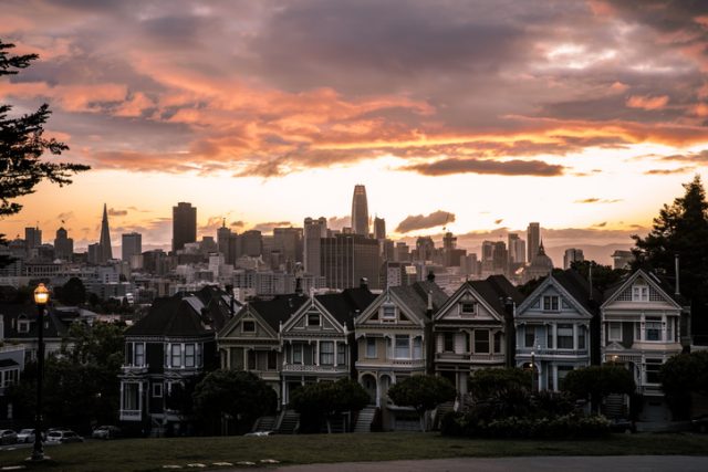 Painted Ladies houses at sunrise in San Francisco, with the city skyline in the background. Colorful clouds.