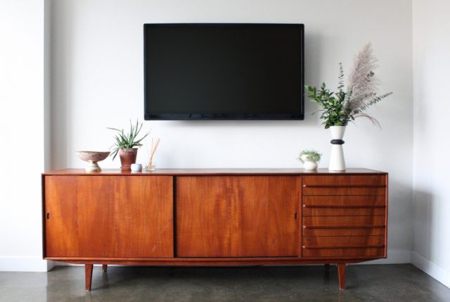 A 50-inch flat screen TV wall is mounted above a mid-century modern teak credenza. Decorated with simple, modern pottery, plants, candle and aromatherapy.