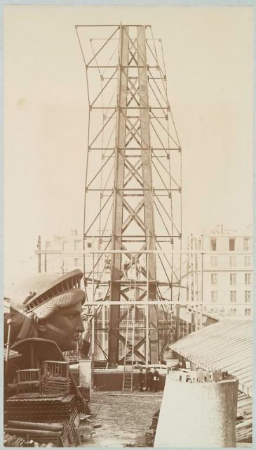 Scaffolding for the assemblage of the Statue of Liberty, of which the head is shown at left, in Paris