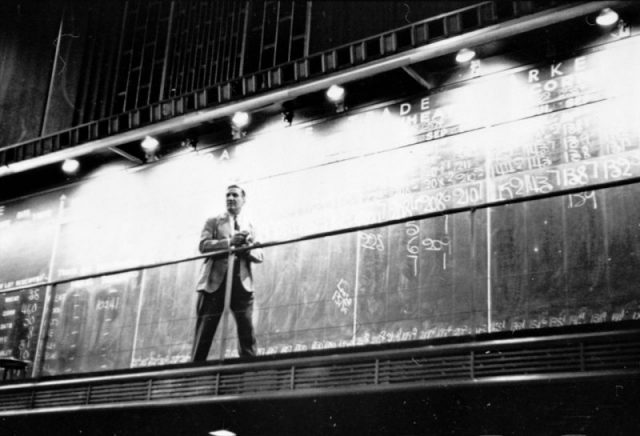 Unidentified man standing in front of a ‘Trade’ board on which he records a ‘Market Score’ at the Chicago Board of Trade. Photography by S. Kubrick.