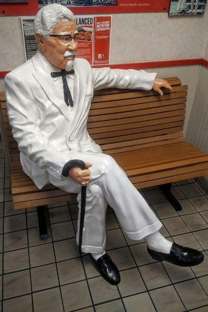 Colonel Sanders statue sitting on bench at KFC in Antioch, CaliforniaPhoto by Checkingfax –CC BY-SA 3.0