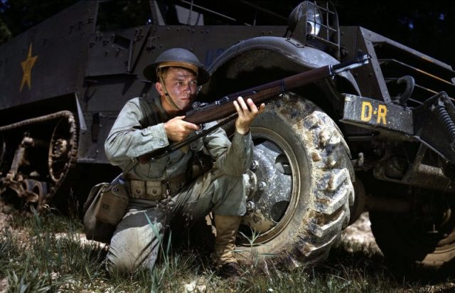 Infantryman wearing Brodie helmet, kneeling in front of M3 Half-track, holds an M1 Garand rifle. Fort Knox, June 1942