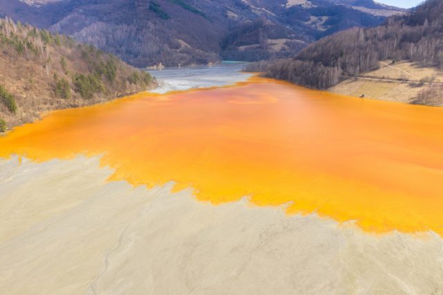 Vividly-colored lake polluted with yellow waste water – aerial view of a mining decanting pond with toxic residuals from copper exploitation. Geamana, Rosia Montana, Romania