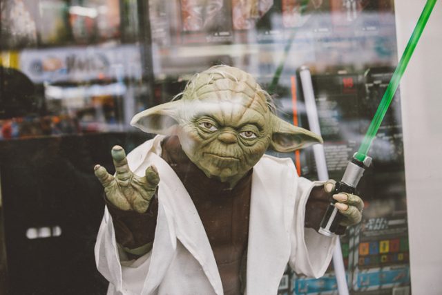 Portrait of Jedi Master Yoda toy model with green lightsaber on window display in Paris