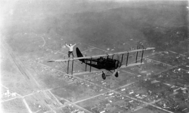 Lillian Boyer, standing on the wing of a flying biplane.