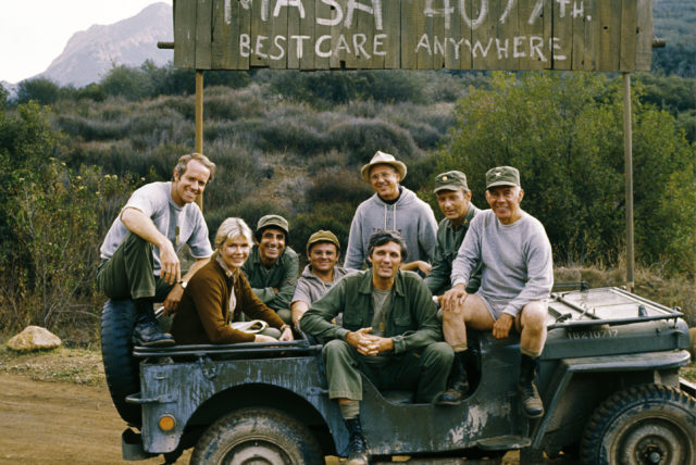 The cast posing in a Jeep
