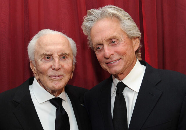 Kirk and Michael Douglas pose before a red curtain