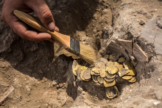 Israeli archaeologist Shahar Krispin cleans gold coins recently discovered at an archeological site in central Israel. The collection of 425 complete gold coins, most dating to the Abbasid period around 1,100 years ago, is considered an ‘extremely rare’ find. Credit: Heidi Levine