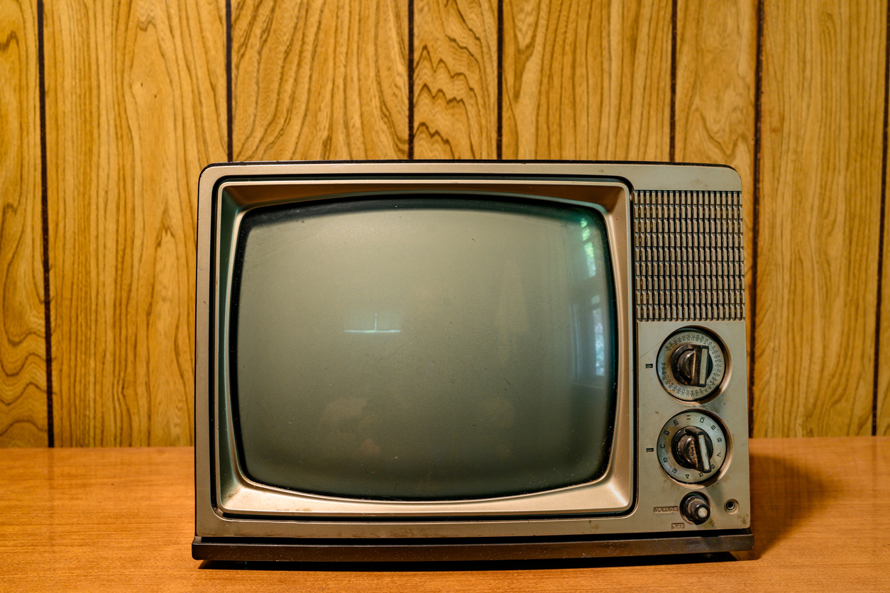 This is a photograph of a small retro television from the 1980s in front of a vintage wood paneled wall.