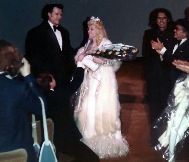 West gives a speech after the Cinerama Dome opening, with Paul Novak, Alice Cooper, Harry E. Weiss and (kneeling in front of her) Dom DeLuise