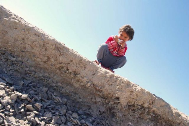 A child in Chahak perched above an archaeological layer where remnants of steel-making were found. Rahil Alipour. Credit: University College London