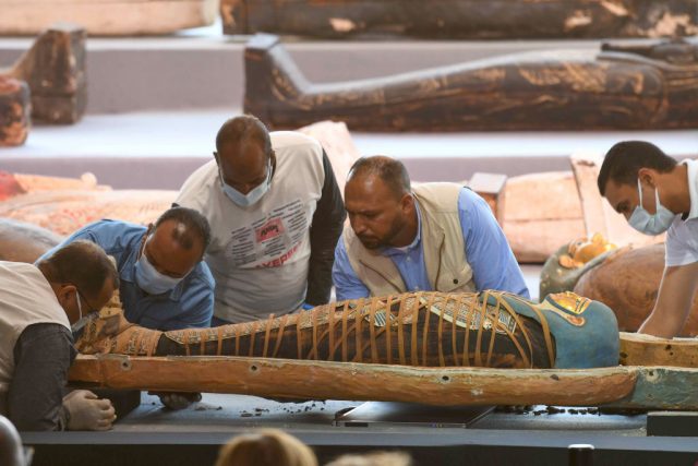 Archaeologists inspect a mummy, wrapped in a burial shroud adorned with brightly coloured hieroglyphic pictorial. Getty Images