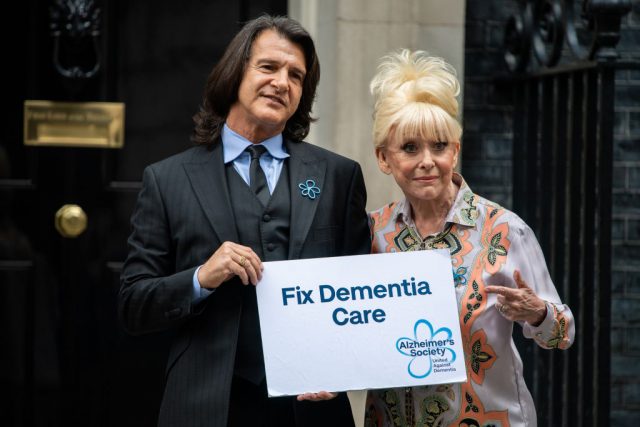 Barbara Windsor and her husband Scott Mitchell holding up a "Fix Dementia Care" sign