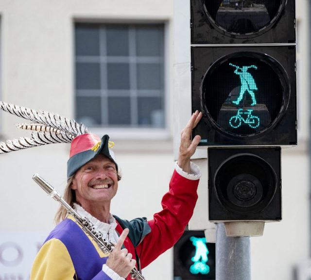The Pied Piper of Hameln, represented by Michael Boyer, smiles next to the Pied Piper traffic light in Hameln. 
