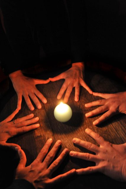 hands joined around a candle for a seance